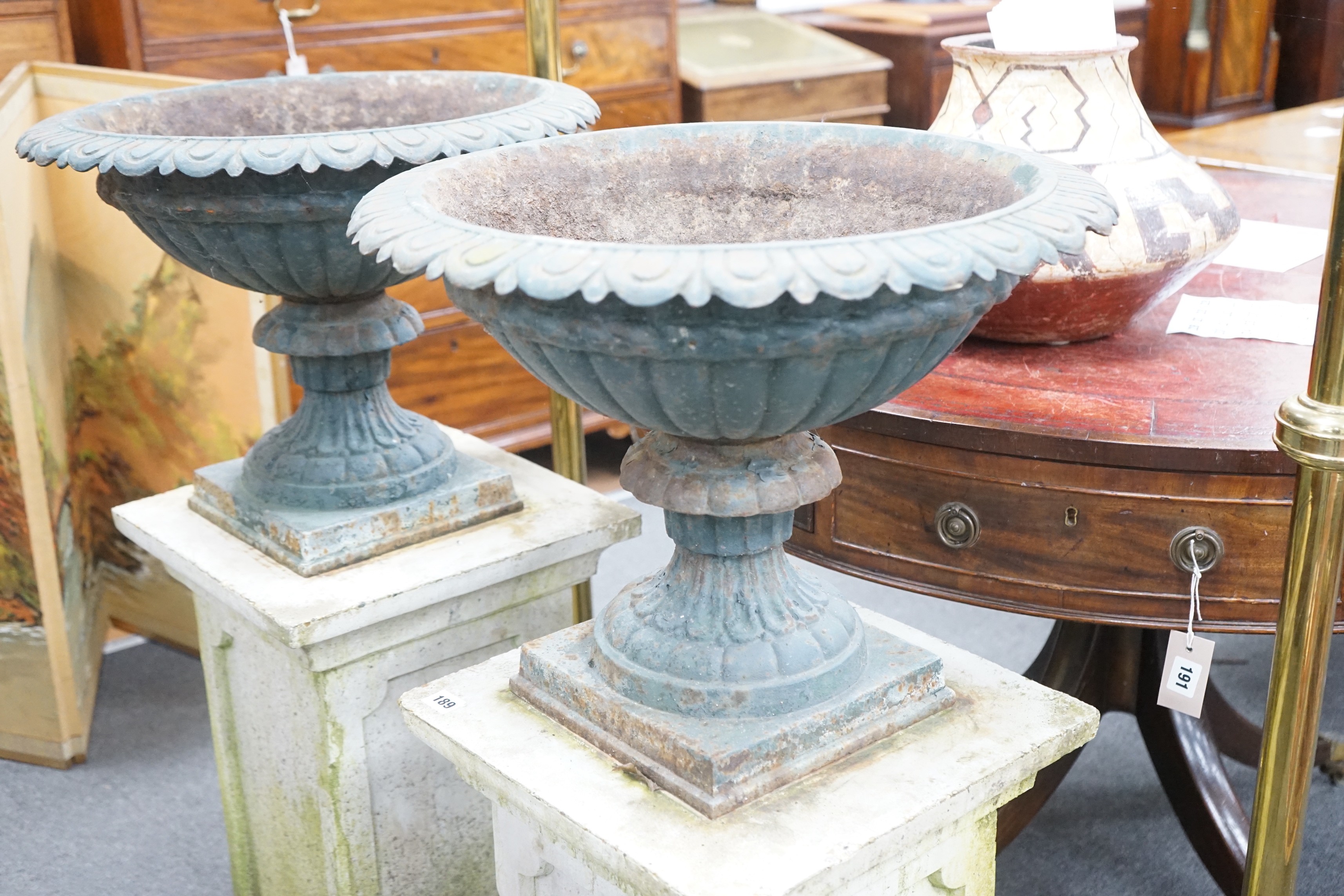 A pair of Victorian painted cast iron campana garden urns on square stone plinths, diameter 51cm, height including plinths 99cm